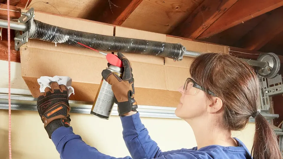 Person applying lubricant to a garage door track to ensure smooth operation.