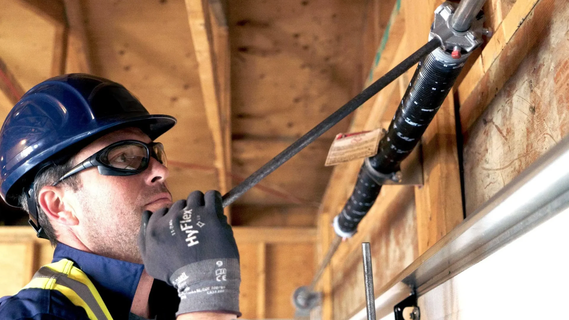 Technician repairing a garage door spring with tools in a residential garage.